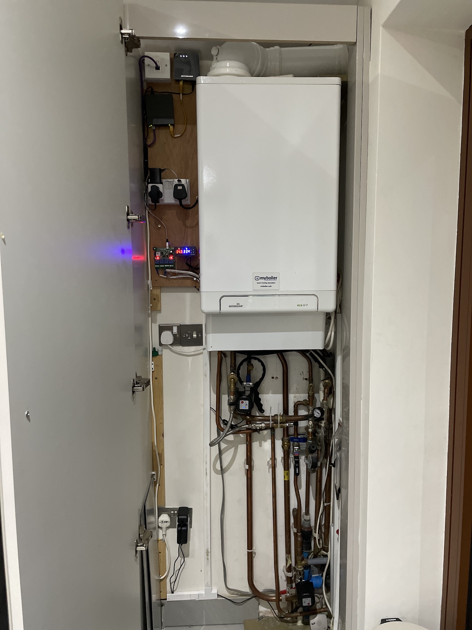 Intergas combi in a cupboard with home-automation relays, Wi-Fi valves, and copper pipework below the case